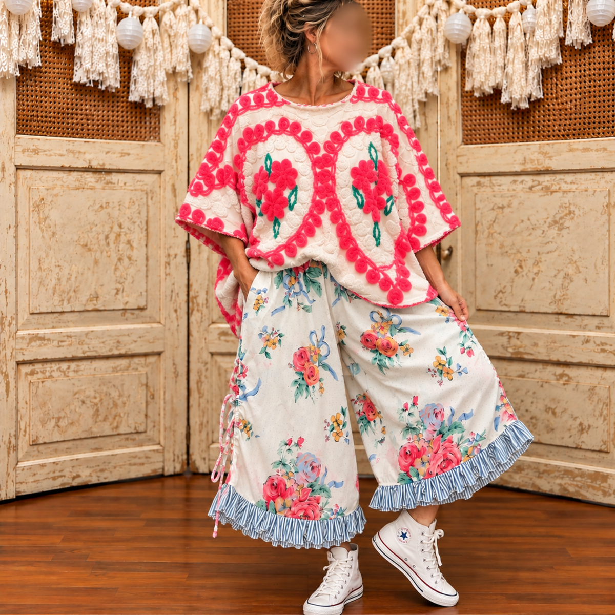 Model wearing a cream tufted chenille top with hot pink scalloped edges and pink posy bouquets, styled with floral wide-leg pants and white sneakers